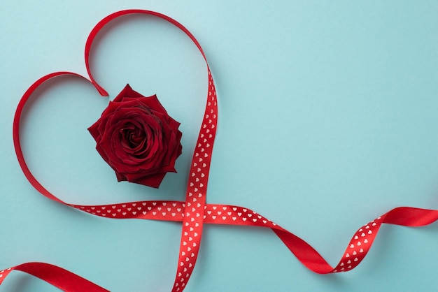 Top view photo of valentine's day decorations red rose in red ribbon heart on isolated pastel blue background with blank space