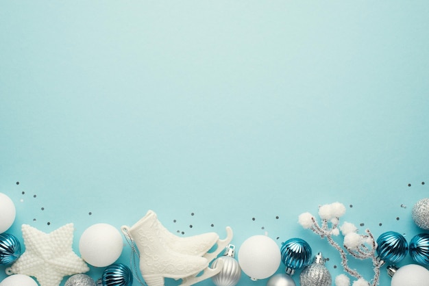 Top view photo of white blue and silver christmas tree decorations star balls sequins ice skates and snowy branch on isolated pastel blue background with copyspace