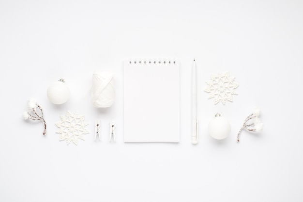 Top view photo of white christmas tree decorations notepad pen snowflakes balls snow twigs spool of thread and clothespins on isolated white background with copyspace