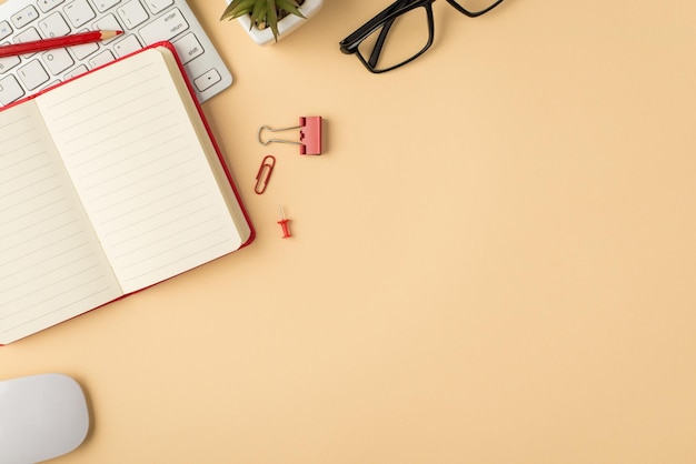 Top view photo of white keyboard mouse flowerpot glasses open red planner pencil binder clip and pin on isolated beige background with copyspace