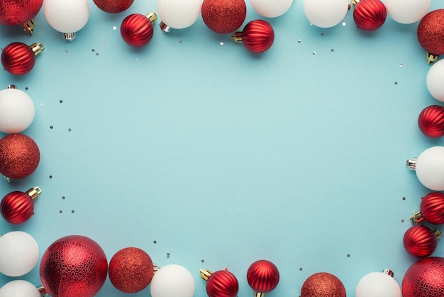 Top view photo of white and red christmas tree balls and sequins on isolated pastel blue background with copyspace in the middle