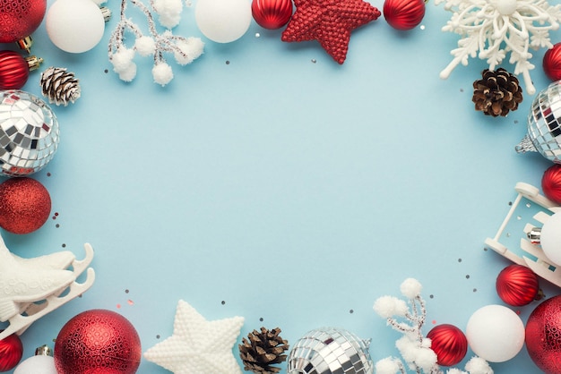 Top view photo of white and red christmas tree decorations disco balls stars snowy twigs pine cones snowflake small sled ice skates and sequins on isolated pastel blue background with blank space