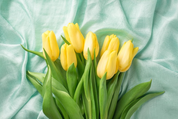 Top view photo of woman's day composition bouquet of yellow tulips on textured pastel blue cloth background