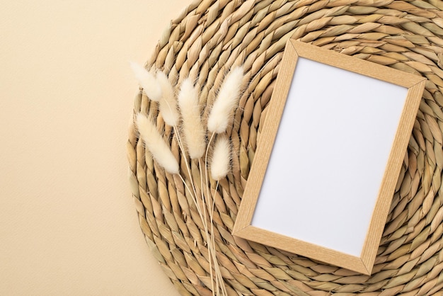 Top view photo of wooden photo frame white lagurus flowers and decorative placemat on isolated beige background with copyspace