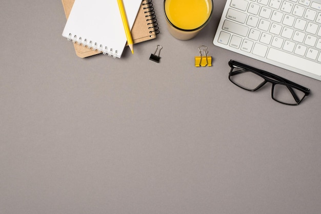 Top view photo of workplace keyboard glass of orange juice glasses binder clips and yellow pencil on reminders on isolated grey background with blank space