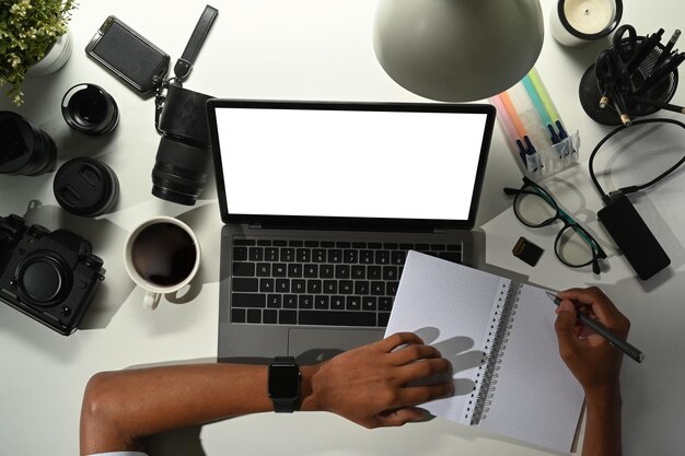 Top view of photographer using laptop and making notes at work station with digital camera memory card and lens