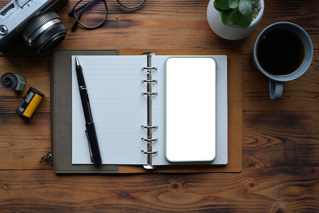 Top view photographer workspace with smart phone notebook and camera on wooden desk