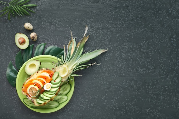 Top view on pinapple boat with smoked salmon and avocado slices with lemon and quail egg