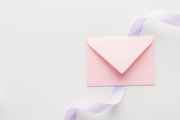 Top view of pink envelope and purple silk ribbon on grey background