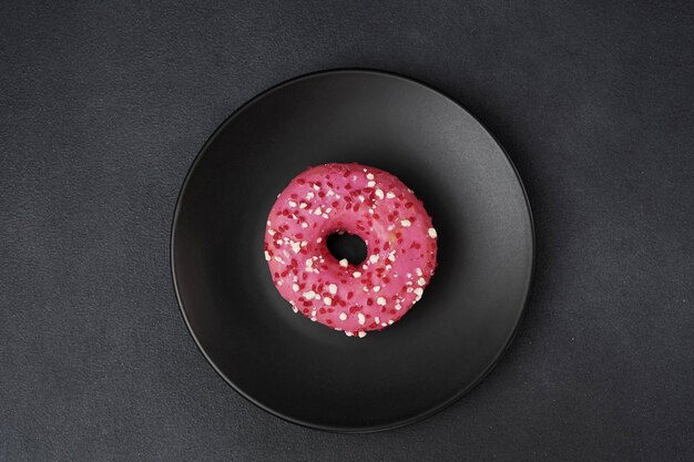 Photo top view of a pink glazed doughnut with colorful sprinkles on a black plate