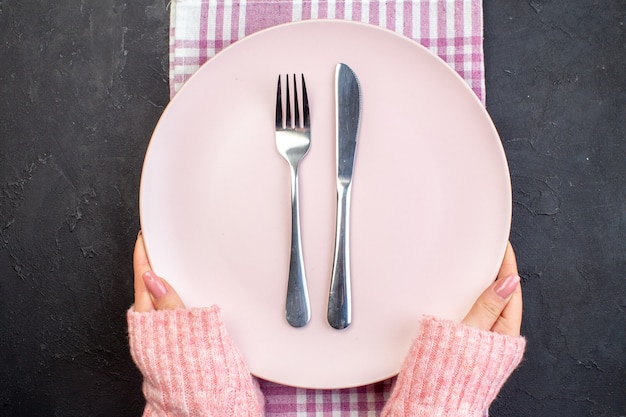 Top view pink plate with fork and knife on dark surface