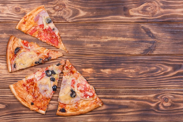 Top View of Pizza Slices with Tomato, Black Olives, Ham and Onion on a wooden table background