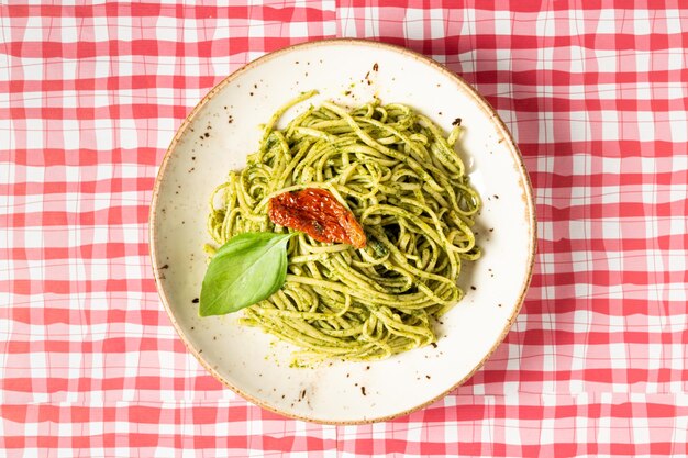 Top view of a plate of spaghetti with pesto sauce on a red and white checkered tablecloth