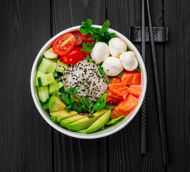 Top view of poke bowl with salmon and avocado on dark background