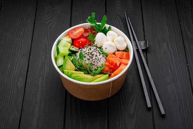 Top view of poke bowl with salmon and avocado on dark background