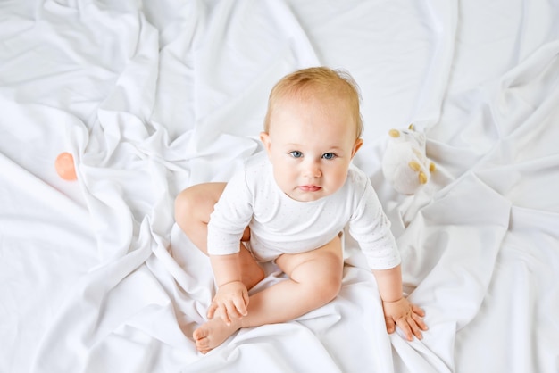 Top view portrait of adorable little baby girl child toddler sitting on bed and attentively looking