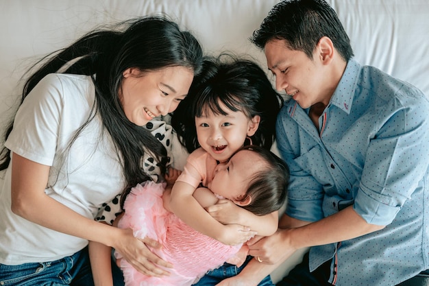 Top view Portrait of happy family is having fun in bedroom Enjoying being together Parents are hugging their little baby while lying in bedWeekend activity happy family lifestyle concept