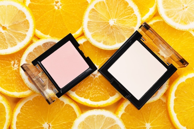 Top view of powder and highlighter. Cosmetics product for facial skin. Maquillage, cosmetic and visagist concept. Place for text or design, flat lay. Yummy slices of orange and lemon on background.