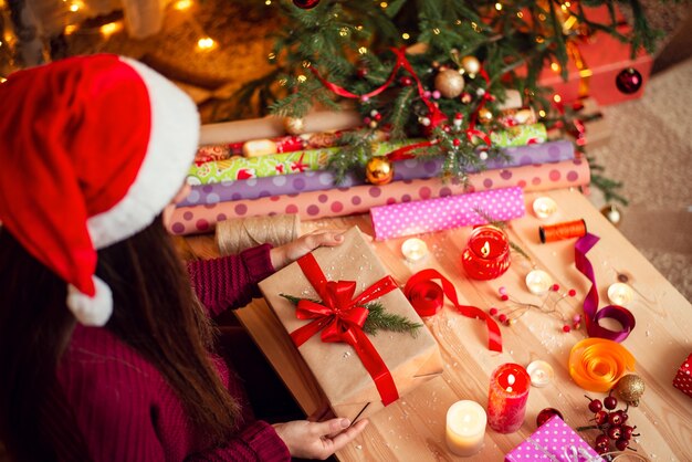 Top view of a present in girl's hands on wooden table with christmas decoration