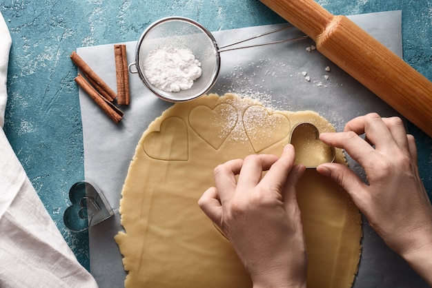 Top view of process of shaping hearts on cookie dough on blue background with kitchen accessories