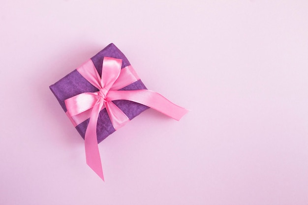 Top view of purple gift box with tied pink bow on the pink background. Copy space.