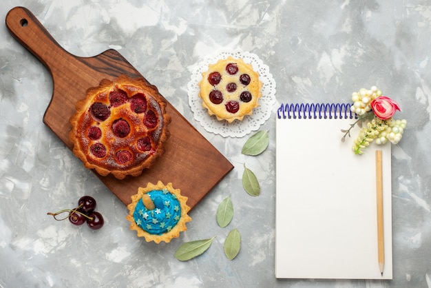 Top view raspberry cake with little cake along with notepad on the light table cake pie cherry fruit sweet