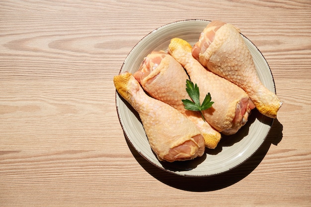 Top view of a raw chicken legs and parsley on a plate on a wooden table next to a window and copy space