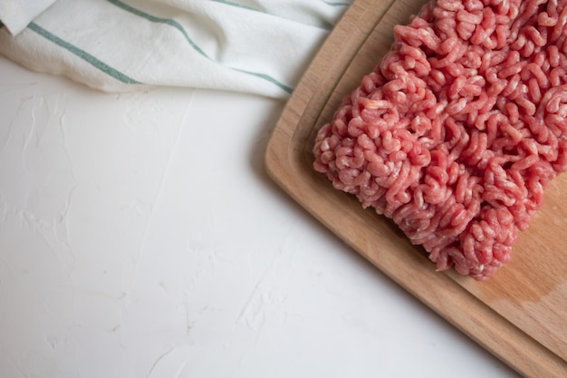 Photo top view raw minced meat on the cutting board and kitchen towel on a white table