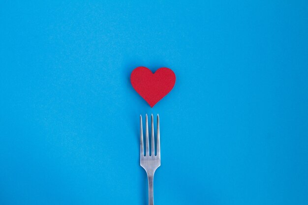 Top view of red heart and fork on the blue