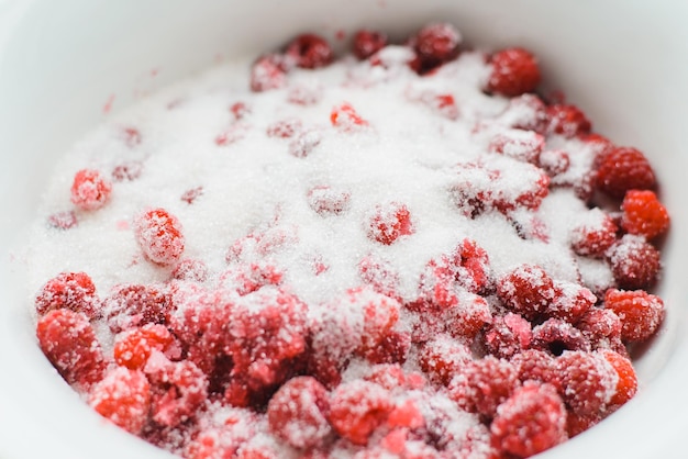 Top view red ripe raspberries covered with sugar in white bowl closeup Process of making raspberry jam