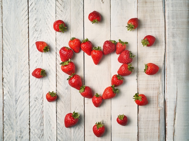 Top view of red strawberries forming a heart on a white wooden table. Concept of love and couple.