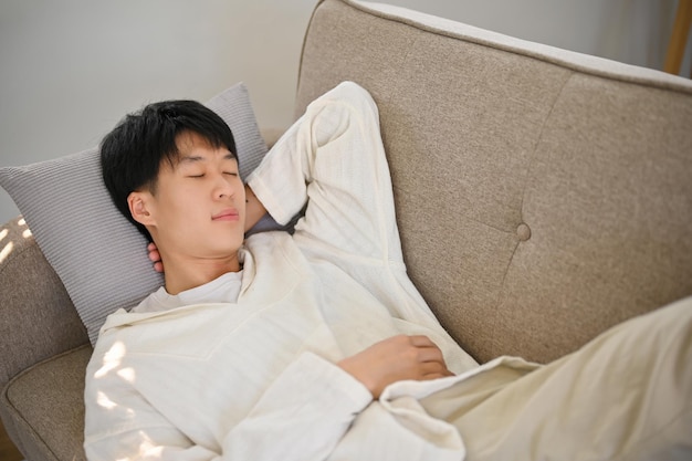 Top view of a relaxed and calm young Asian man in comfy clothes sleeping on the sofa