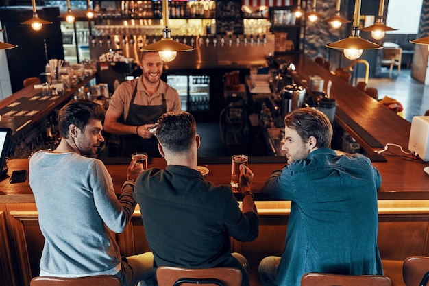 Top view of relaxed young men in casual clothing drinking beer while sitting in the pub