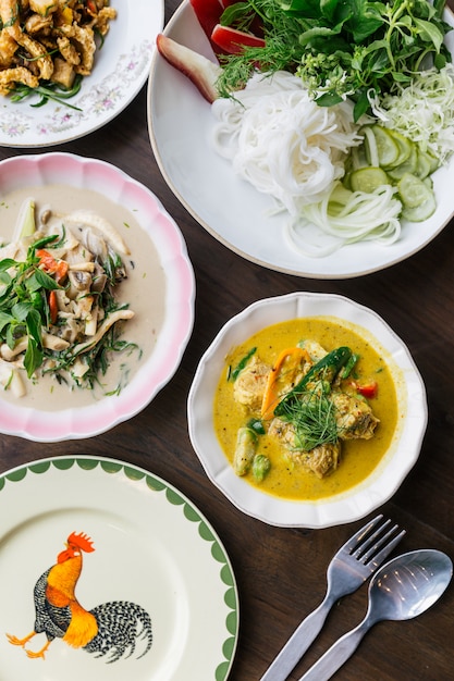 Top view of Rice Noodles with Crab Meat Curry Sauce, Served with vegetables. Stir Fried Spicy Minced Pork with Herbs. Spicy Crispy Pork Skin and Mushroom Soup. Classic Thai cuisine with steam rice.