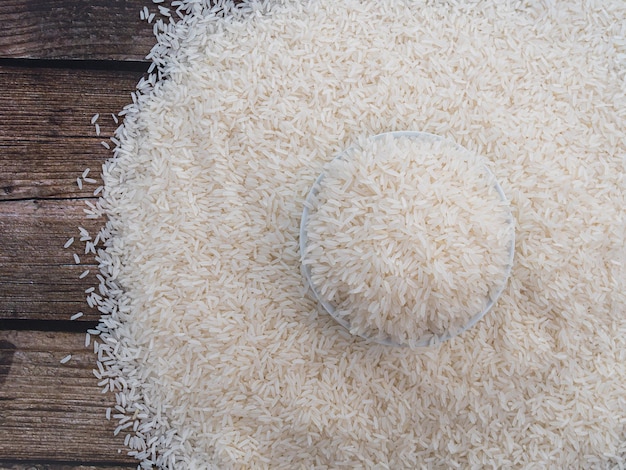 Top view rice in a white bowl and scattered near on wooden table with copy space for text and design