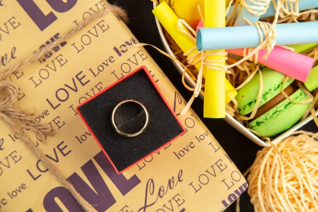 top view ring in box heart box with rolled up sticky notes and macarons wrapped gifts flower bouquet on dark background