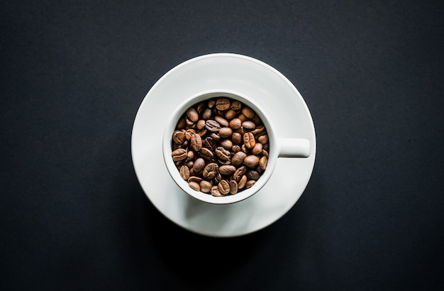 Top view of roasted coffee beans in white coffee cup with black background