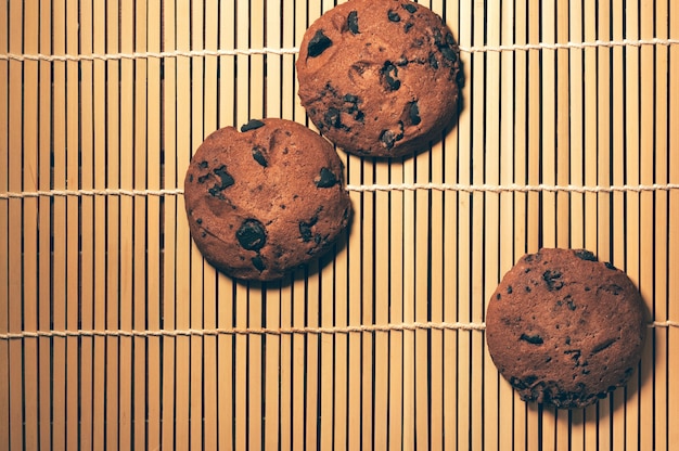 Top view of round crispy chocolate cookies with cocoa chips on textured bamboo background