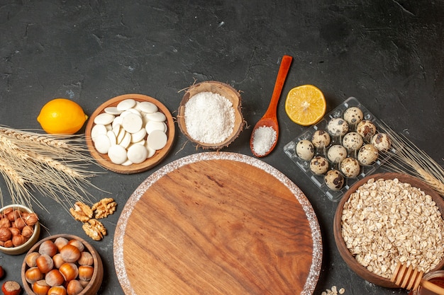 top view round wood board lemon white chocolate rounds coconut powder oats hazelnuts in bowls quail eggs in viol on table