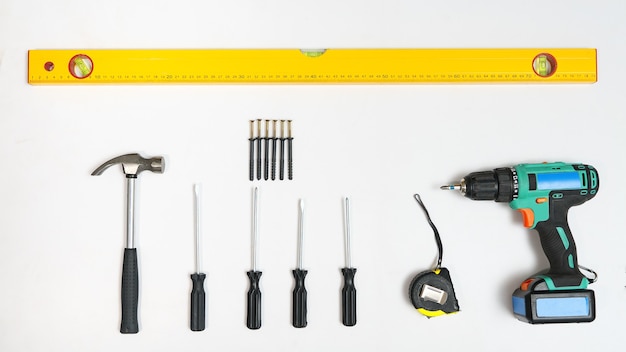 Top view of screwdrivers,hammer, screws, dowels amd ruler on white backdrop.