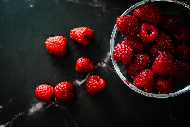 Top view of a serving of raspberries in a small clear bowl on a black granite surface Dark Food horizontal orientation space for text