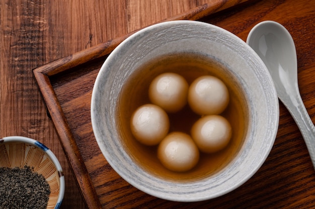 Top view of sesame big tangyuan (tang yuan, glutinous rice dumpling balls) with sweet syrup soup in a bowl on wooden table background for Winter solstice festival food.