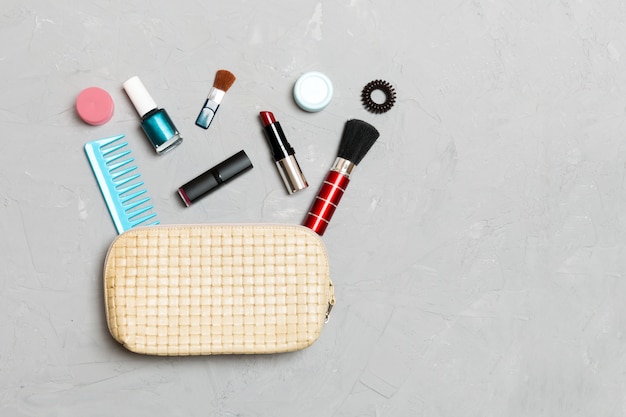 Top view of set of make up and skin care products spilling out of cosmetics bag on cement background