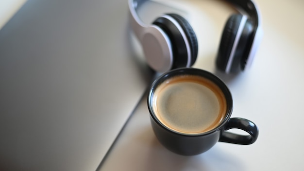 Top view shot of Coffee mug with laptop and headphone on placed on a table in a cafe.