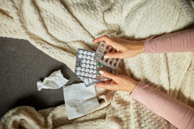 Top view Sick woman looking blister of medicine in hand, while recovering at home, ill woman with pills while sitting on couch at home