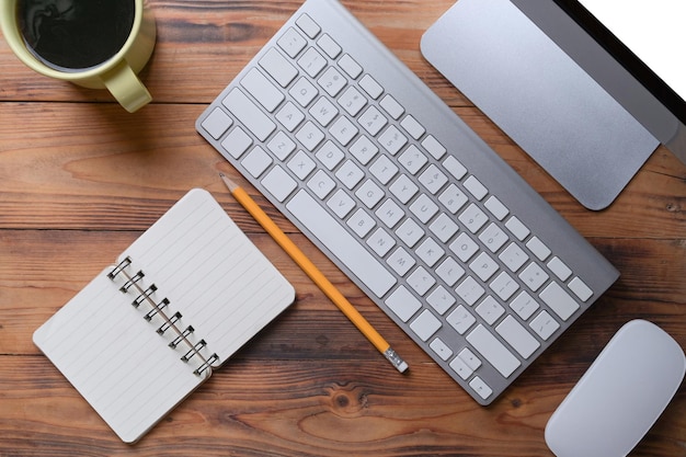 Top view simple workspace with computer wireless keyboard notebook and coffee cup on wooden desk