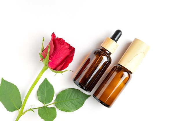 Top view of skin care products in dark glass bottles Dropper with beauty serum or oil face cream and red rose on white background Female skin treatment advertisement