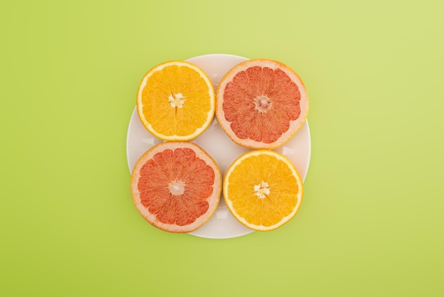 Top view of sliced oranges and grapefruits on white plate isolated on green