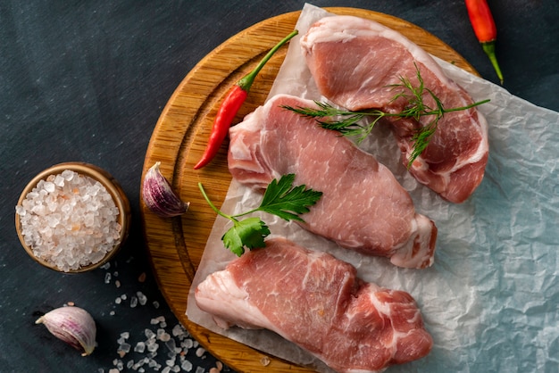 Top view of sliced raw meat on a wooden cutting board with ingredients to cook such as lemon spices and herbss