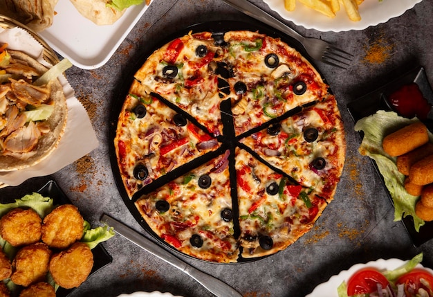 Top view of a sliced vegetable pizza and different assorted dishes